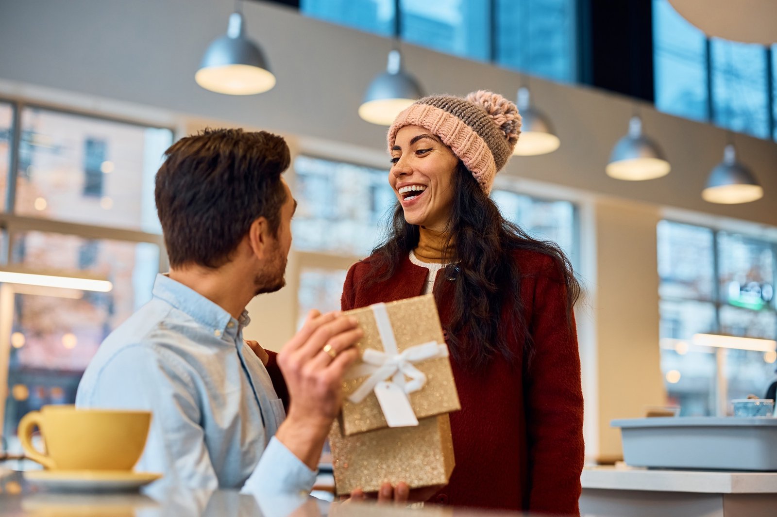 Cheerful woman surprising her boyfriend with a present for their anniversary.